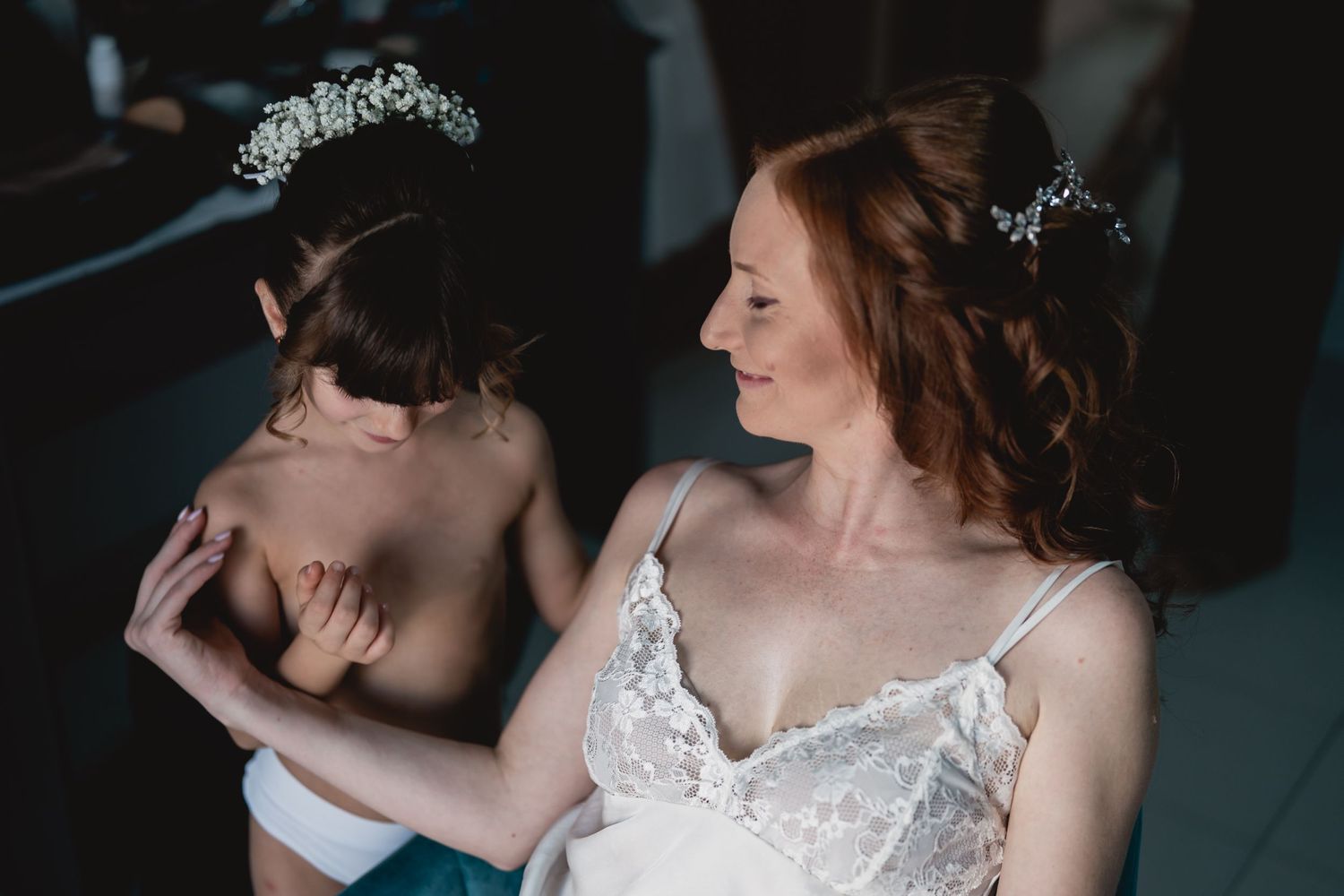 Two people wearing delicate tiaras and white dresses in an intimate moment.