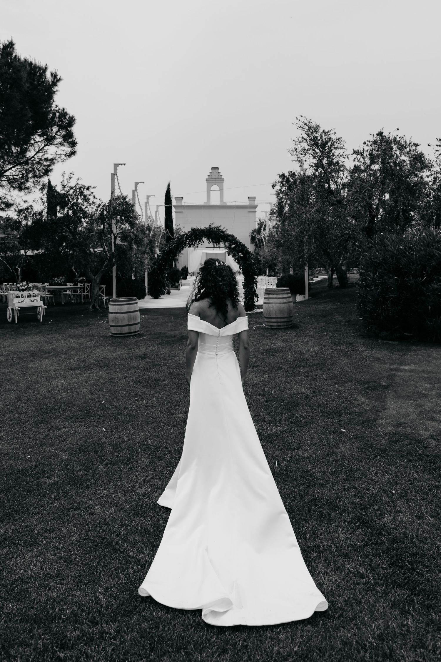 A dramatic black and white photo of a bride in front of a Mediterranean-style building.