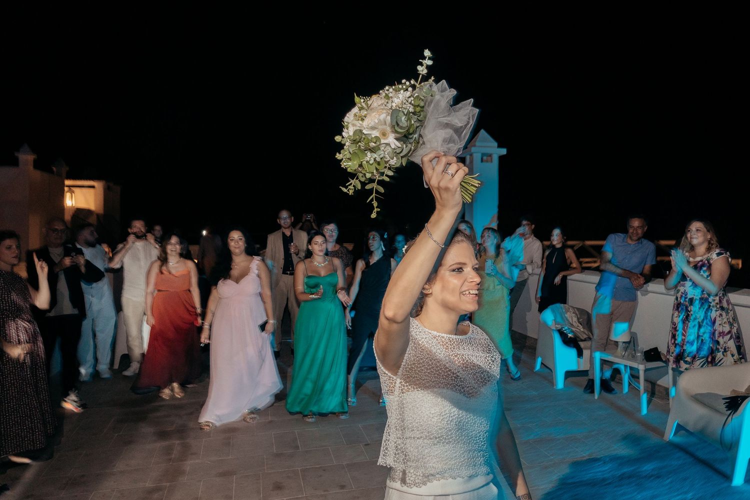 A bride tossing her bouquet during the traditional wedding bouquet toss at night.