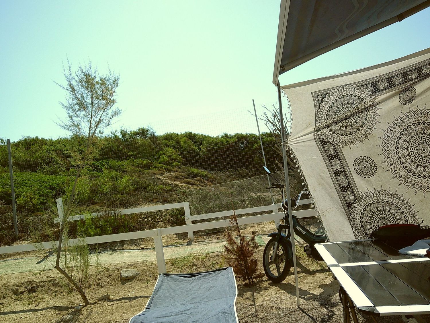 Campsite view showing beach path, bicycle, and decorative tapestry in corner.