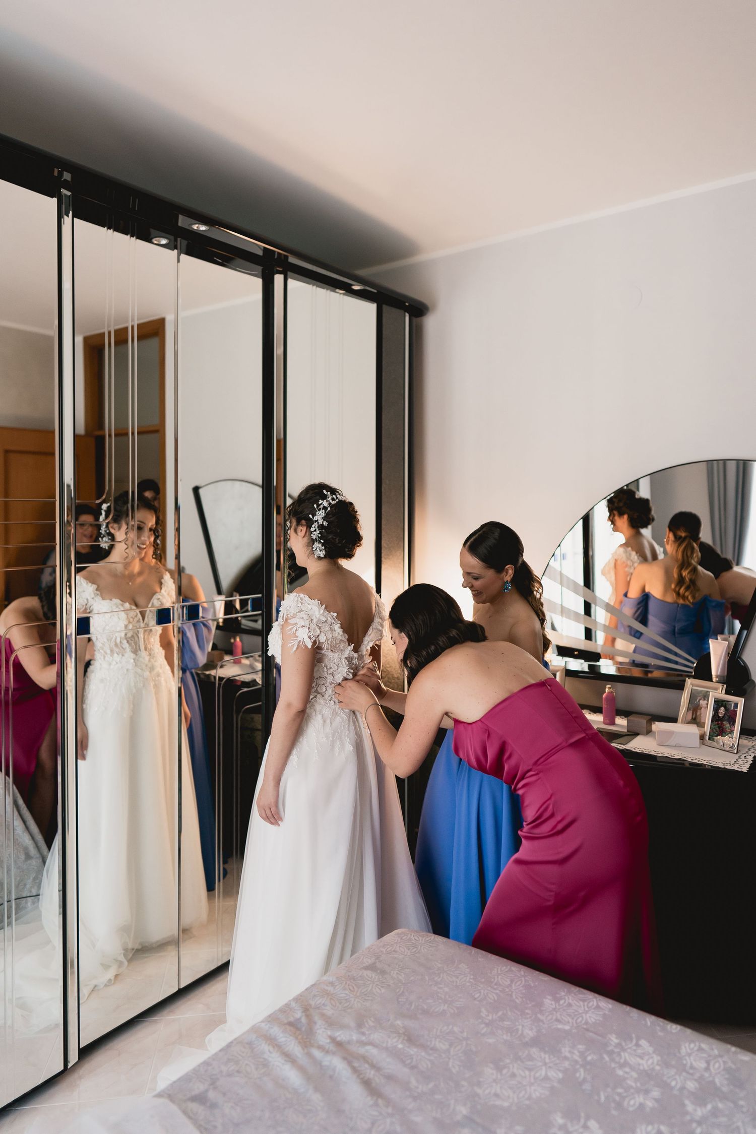 Wedding preparations reflected in mirrored closet doors as attendants help with the bride's dress.