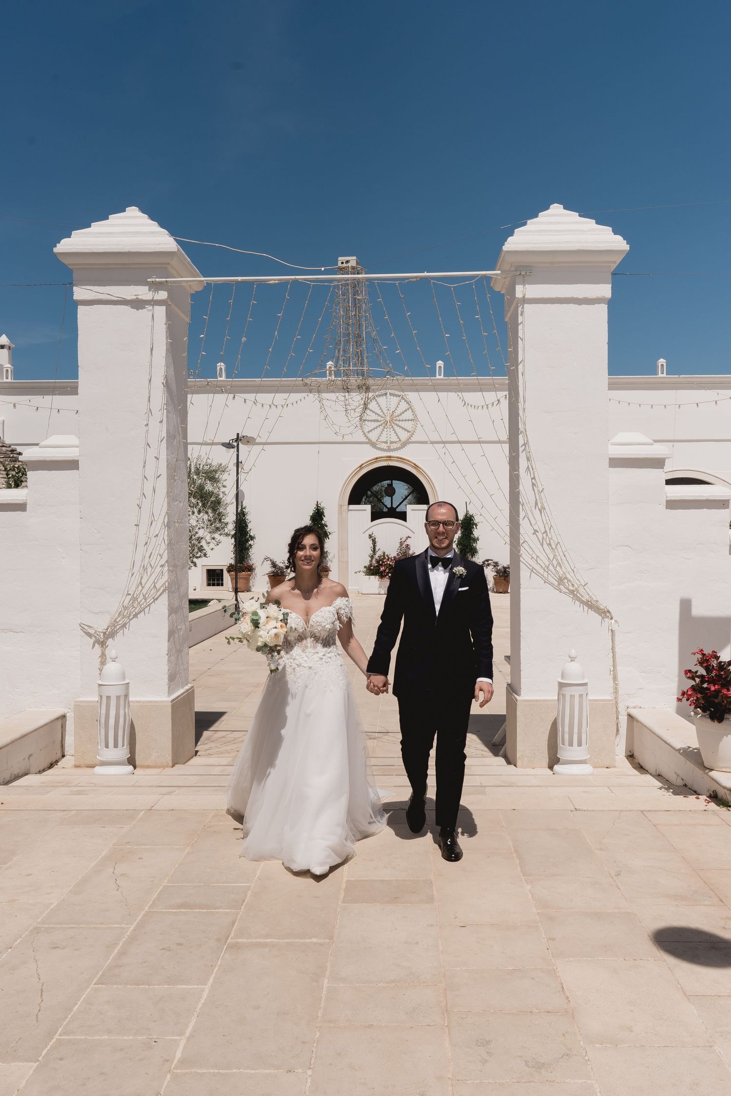 Wedding ceremony entrance with white pillars and string lights at Mediterranean venue.