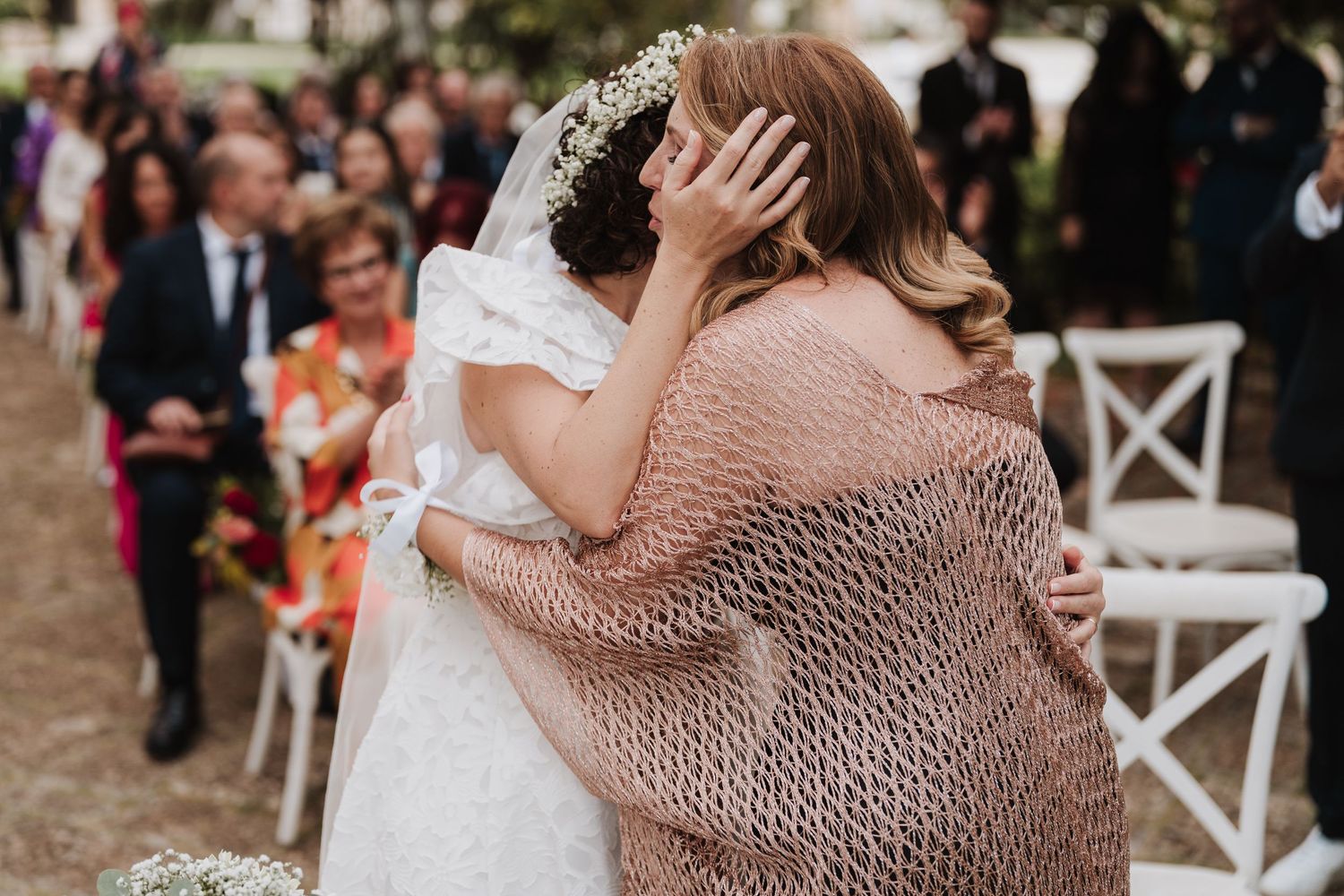 Emotional embrace shared during wedding ceremony with guests looking on.