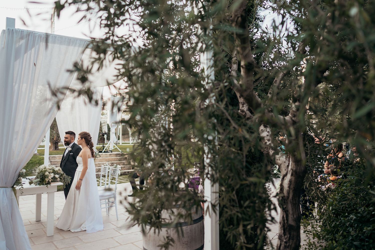 An outdoor wedding venue decorated with white drapes and olive trees creating a romantic atmosphere.