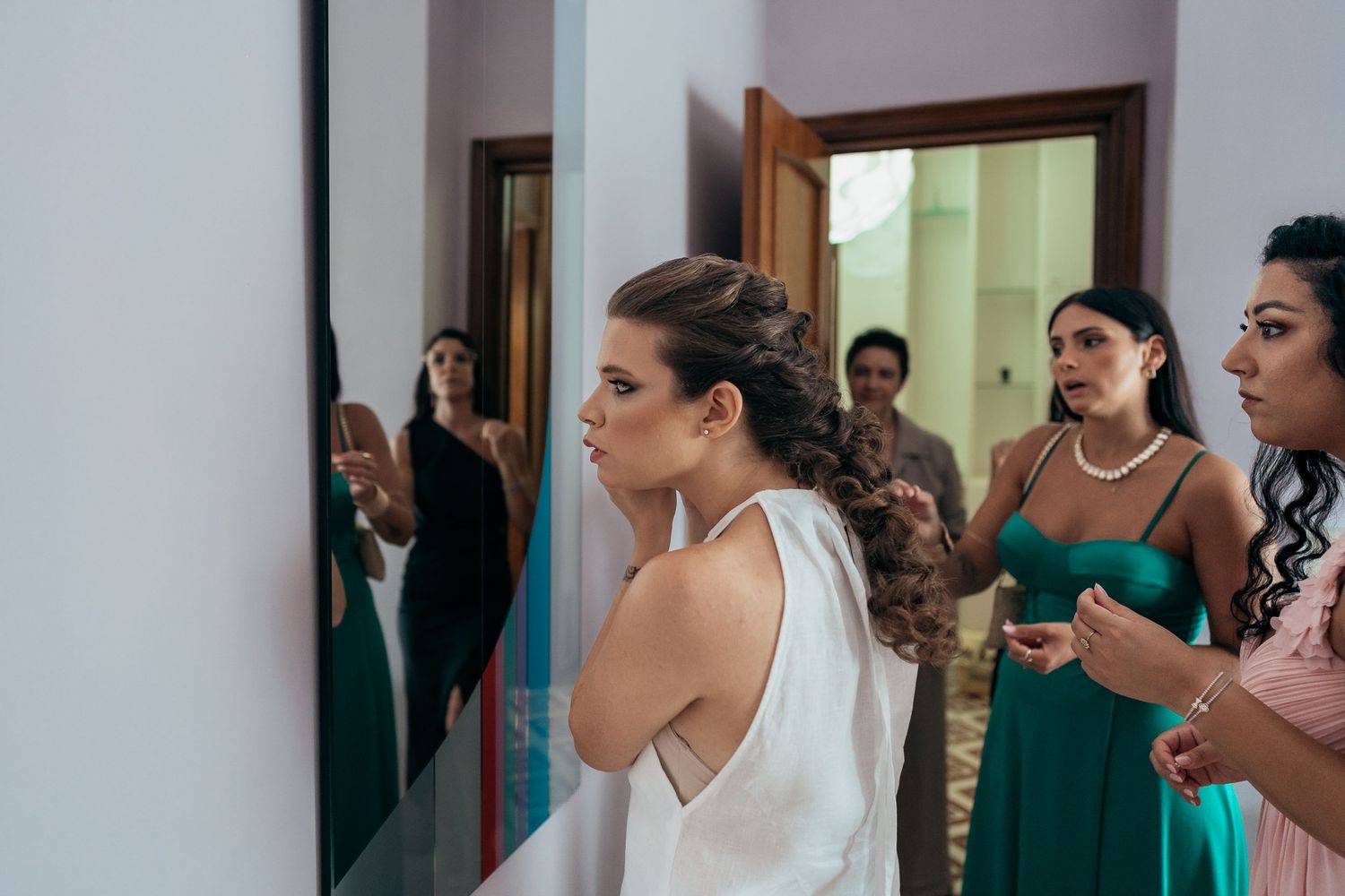 A group of people in formal attire gather in a room with one in a white dress being the focus of attention.