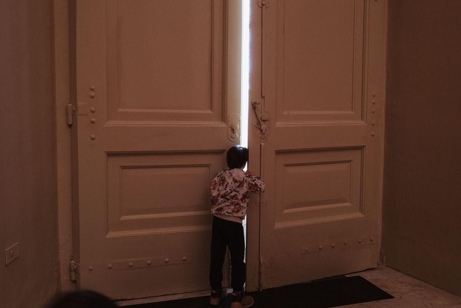 A silhouette peeks through partially opened double doors in a dimly lit interior.