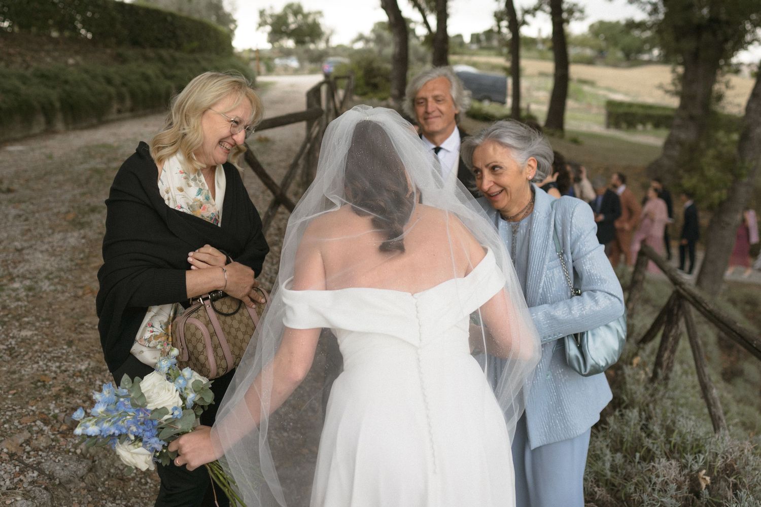 Wedding celebration in a rustic outdoor setting with guests mingling under trees.