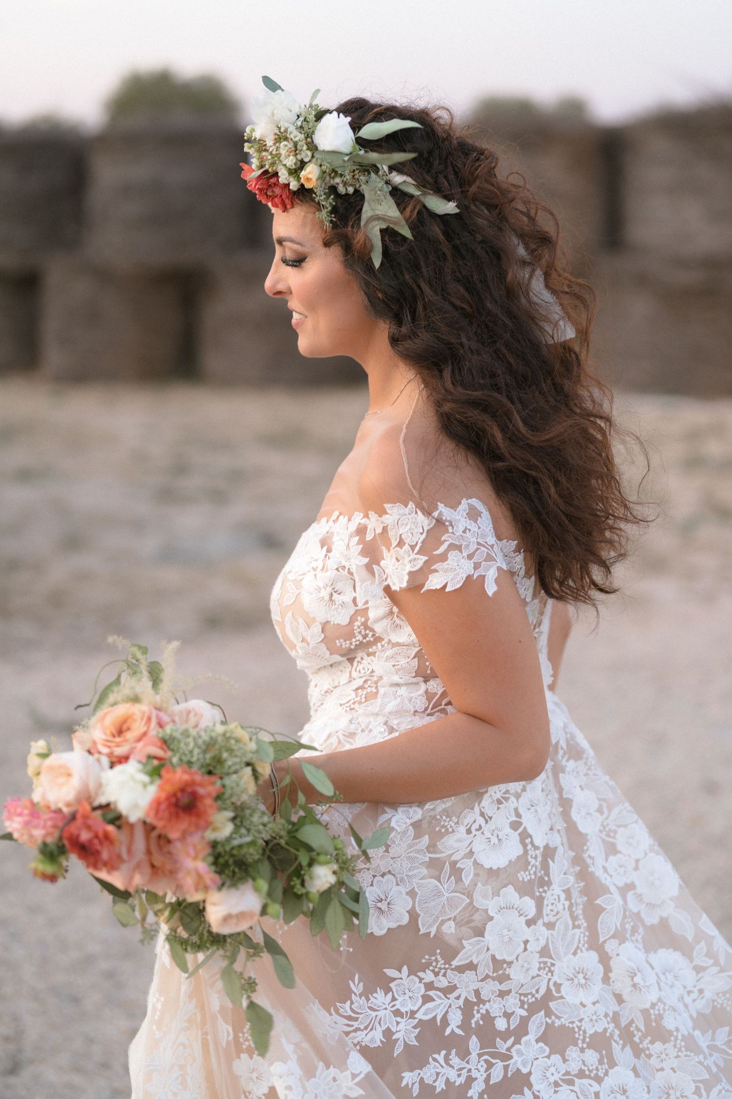 A romantic bridal portrait on the beach shows a flowing white lace dress and floral bouquet in soft peachy tones.