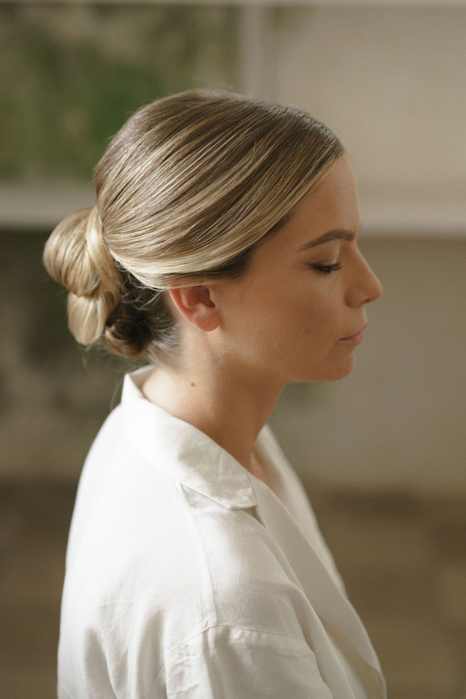 A side profile view of someone in white with an elegant updo hairstyle and soft makeup.