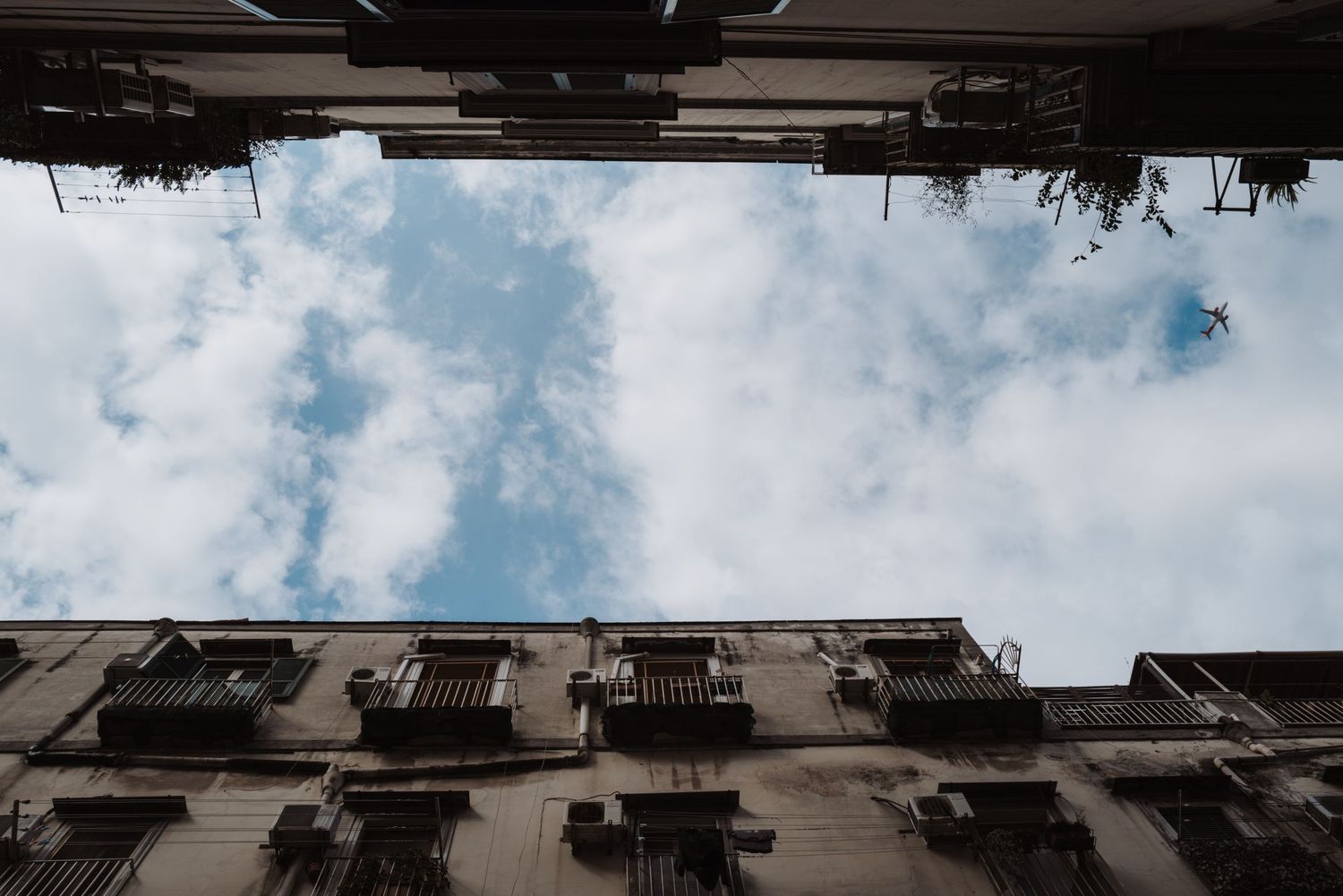 Looking up at historic apartment building facades and balconies against a blue cloudy sky in an urban setting.