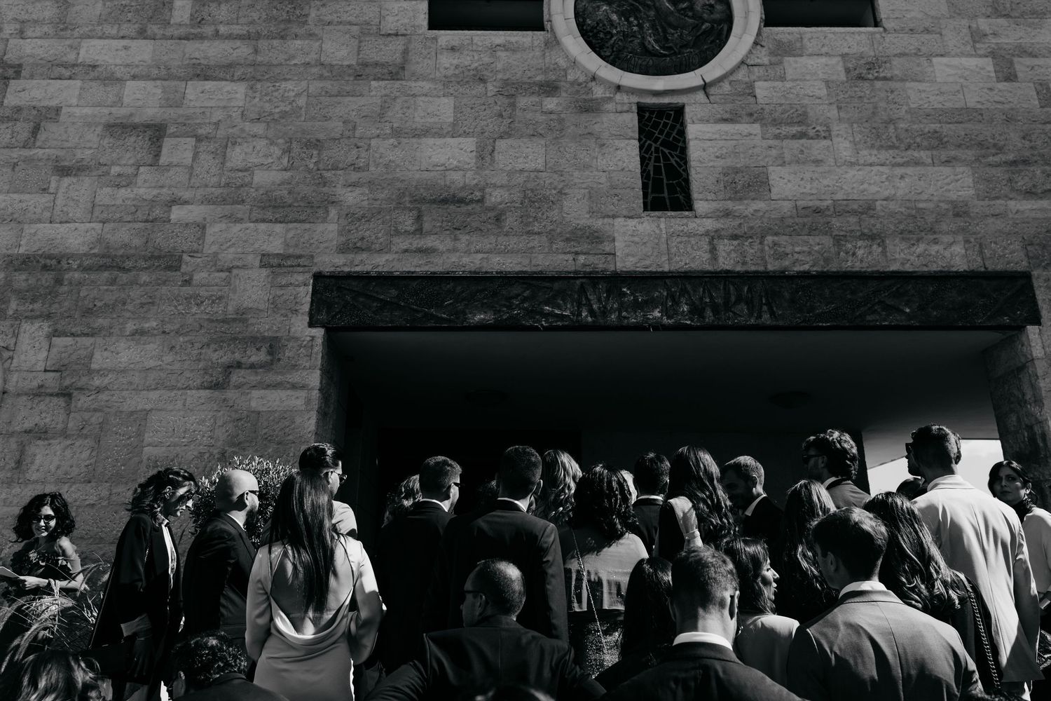 Wedding guests gathering at the entrance of a stone church in black and white photography.