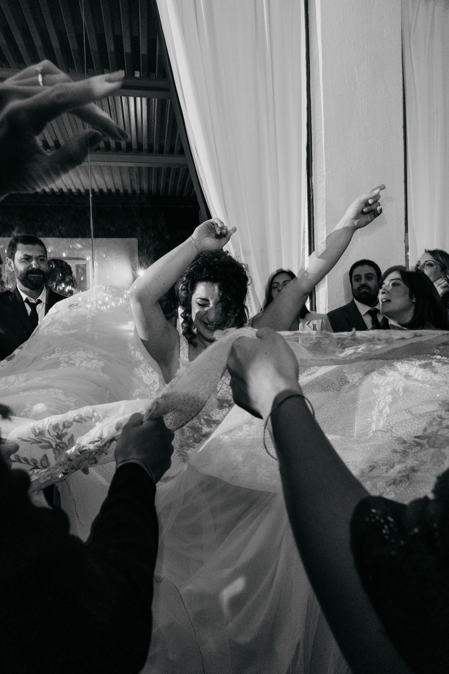 Bride in white wedding gown dances joyfully with arms raised at wedding reception celebration.