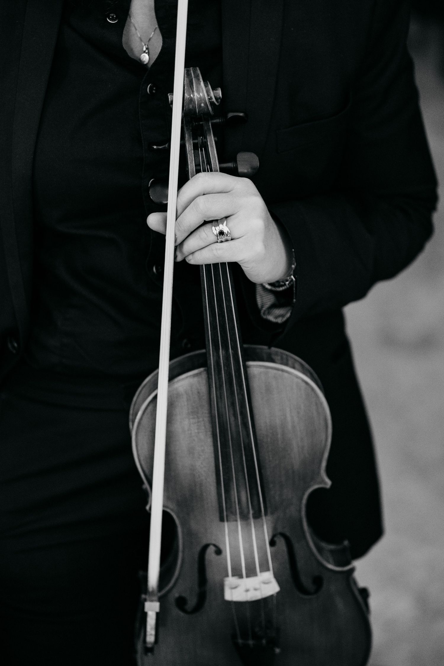 Close-up black and white photo of a musician holding a violin and bow at a wedding.