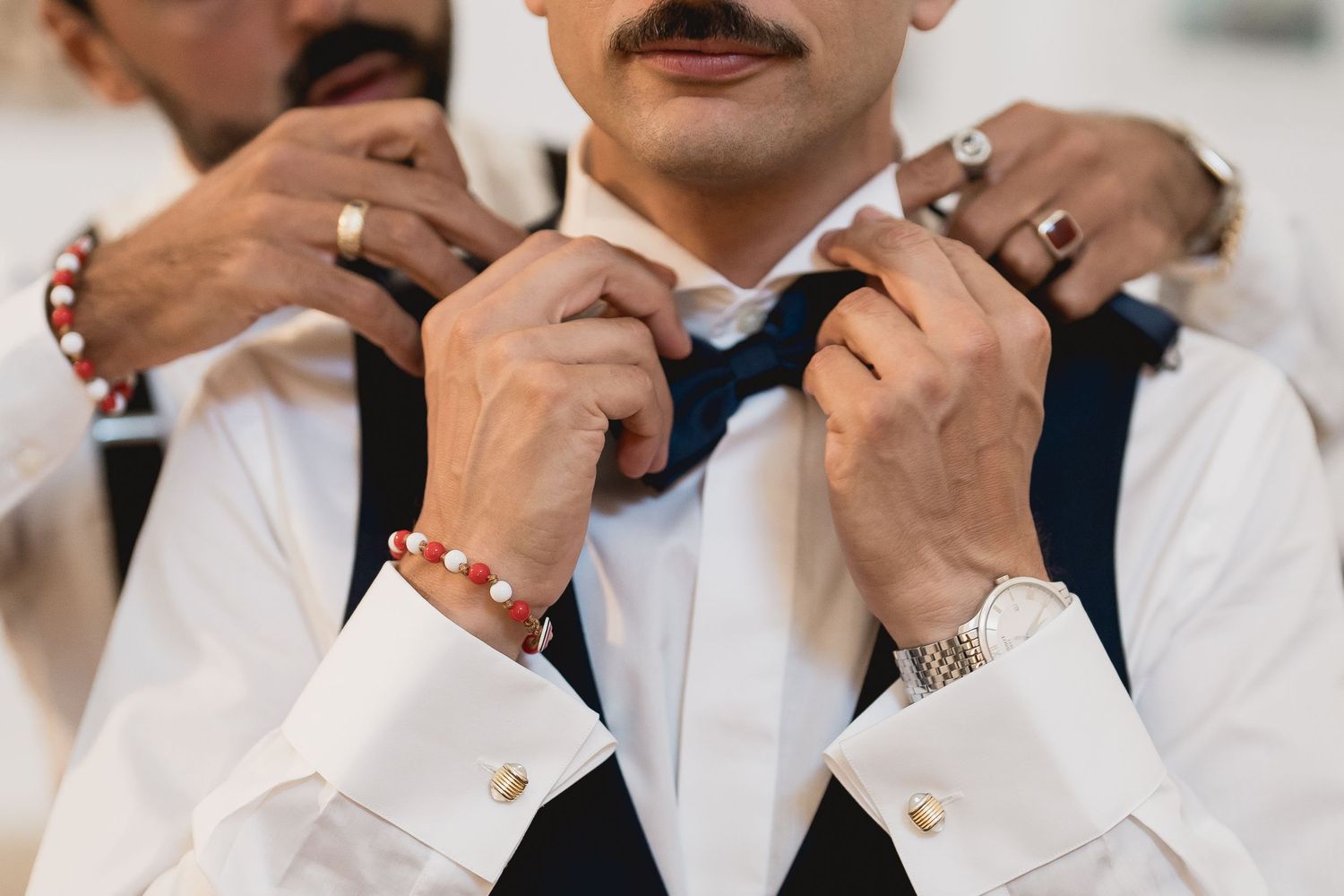 Close-up detail shot of hands adjusting a black bowtie with elegant cufflinks and jewelry.