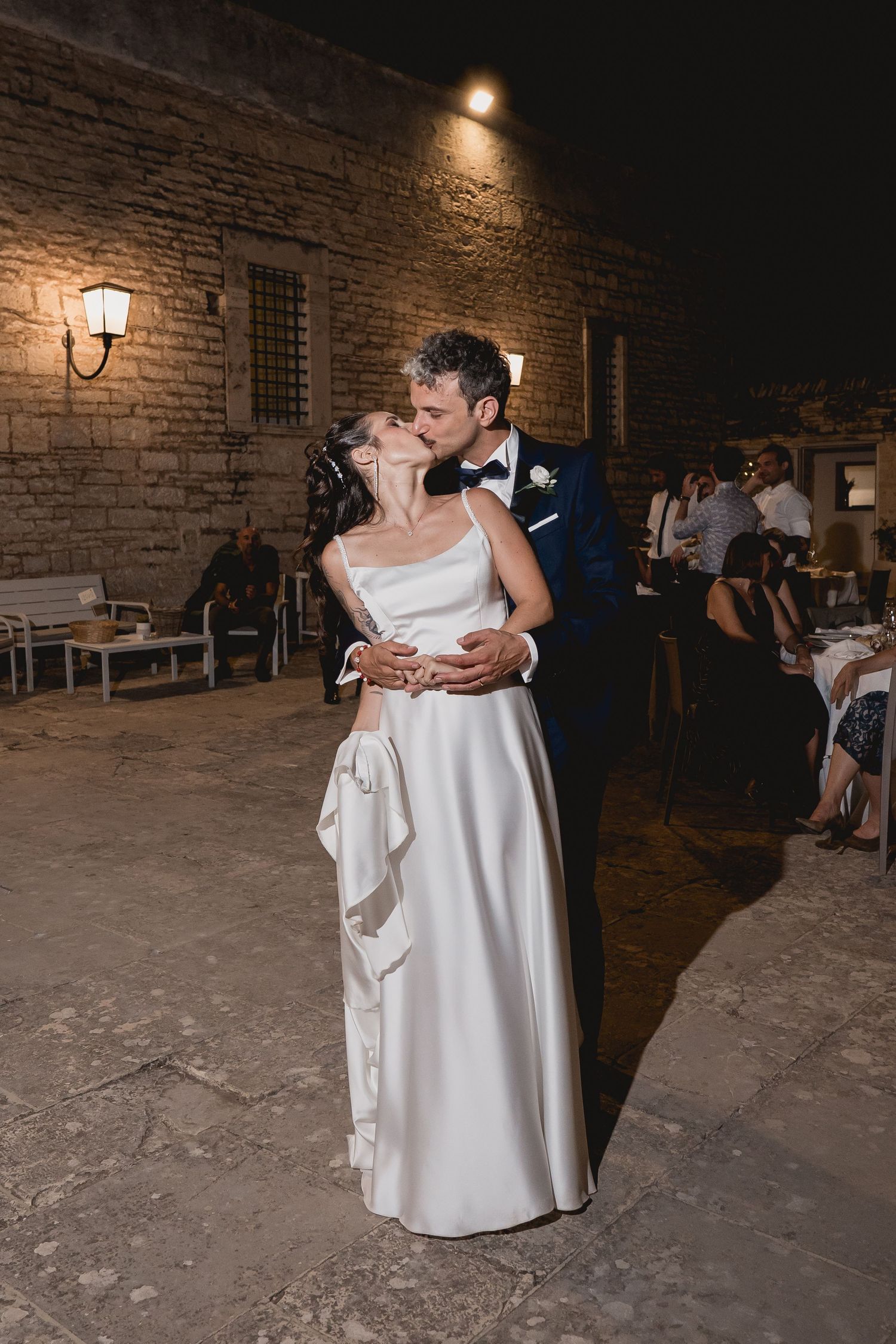 A couple shares their first dance at a rustic wedding reception with stone walls and warm lighting in the background.