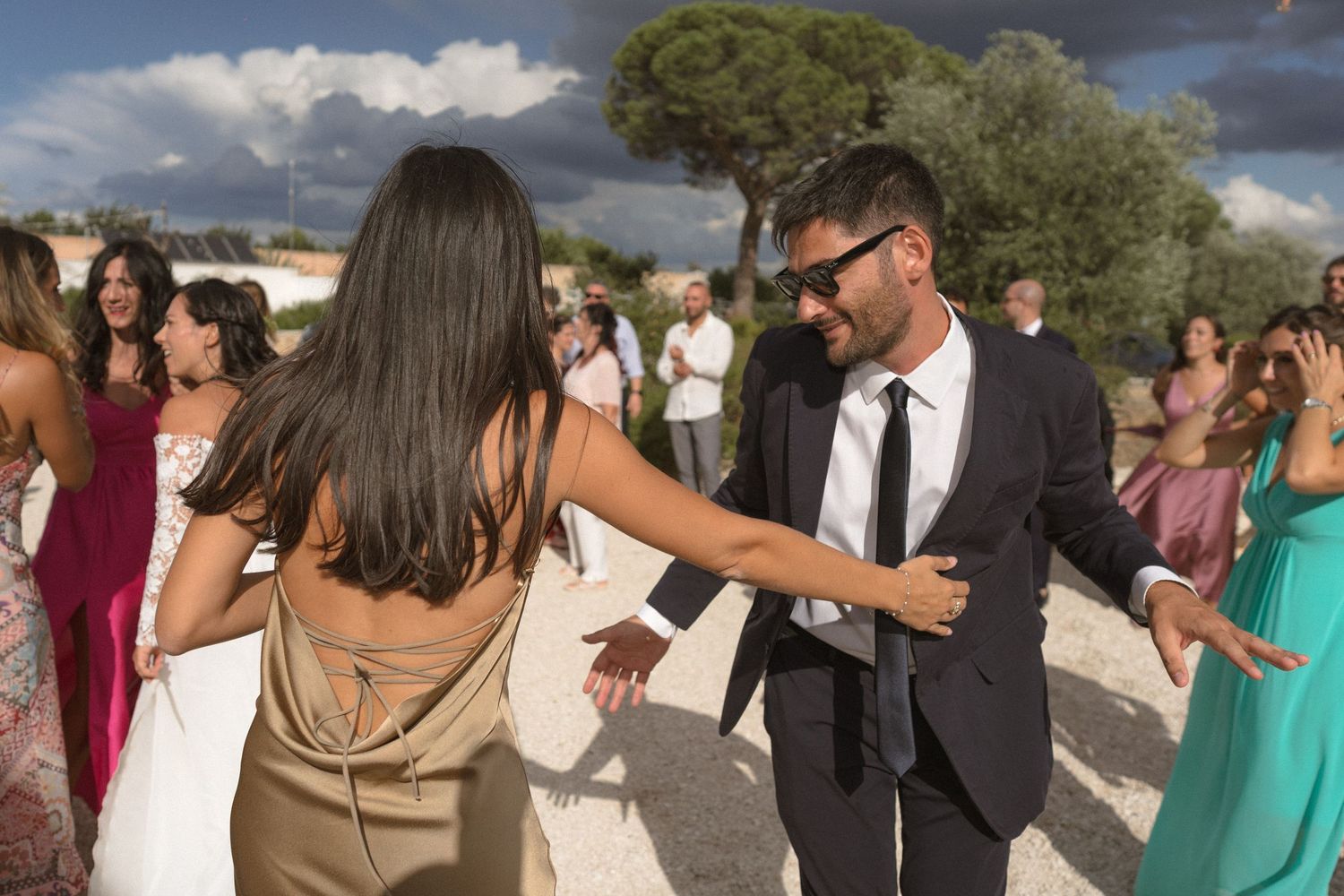 Wedding guests mingling outdoors under a bright blue sky with trees in the background.
