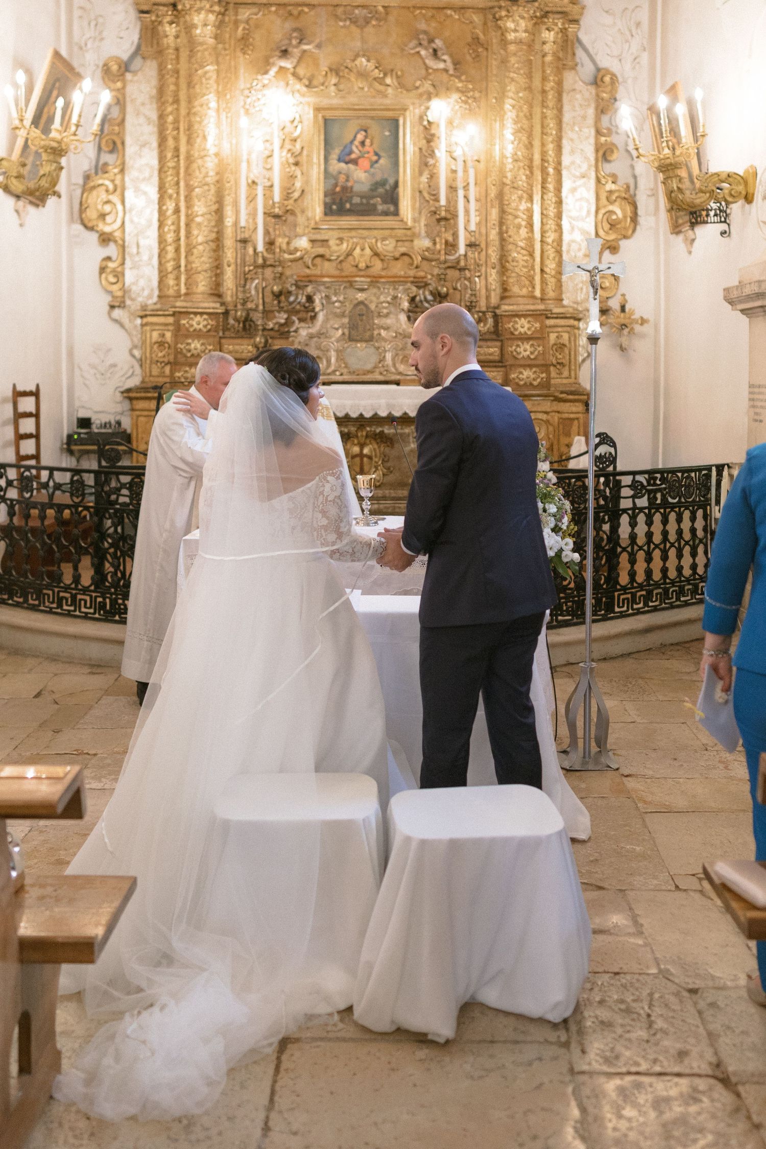 Wedding ceremony in an ornate golden baroque church with chandeliers and decorative details.