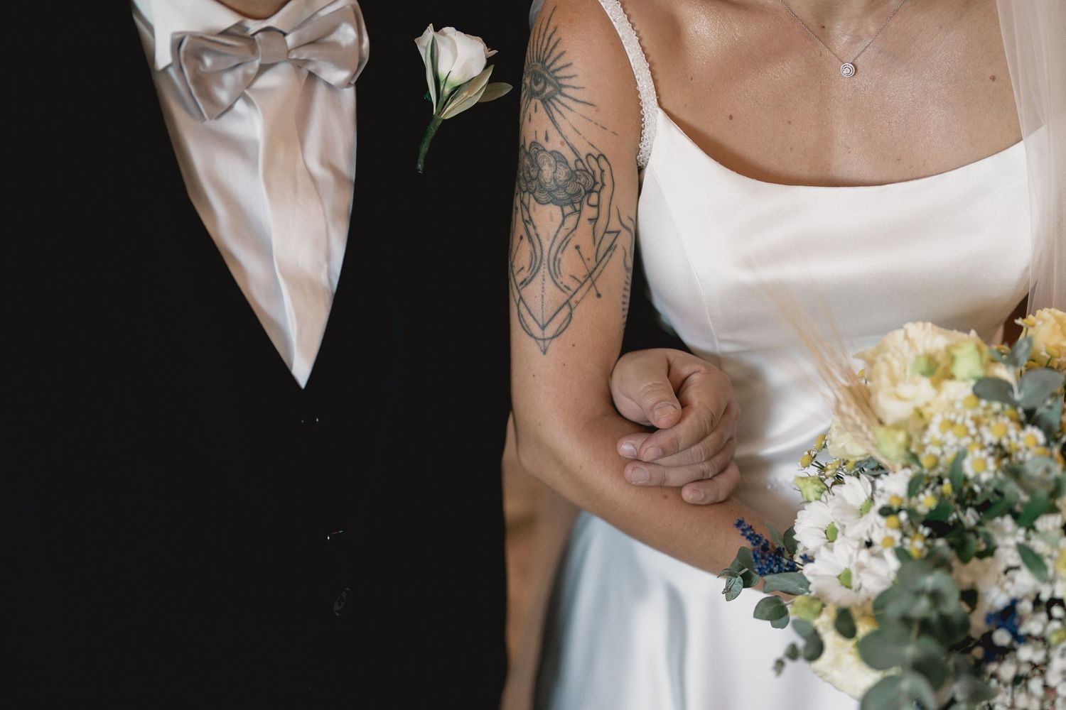 A close-up of a bowtie and bridal details with spring flowers and visible tattoo art.