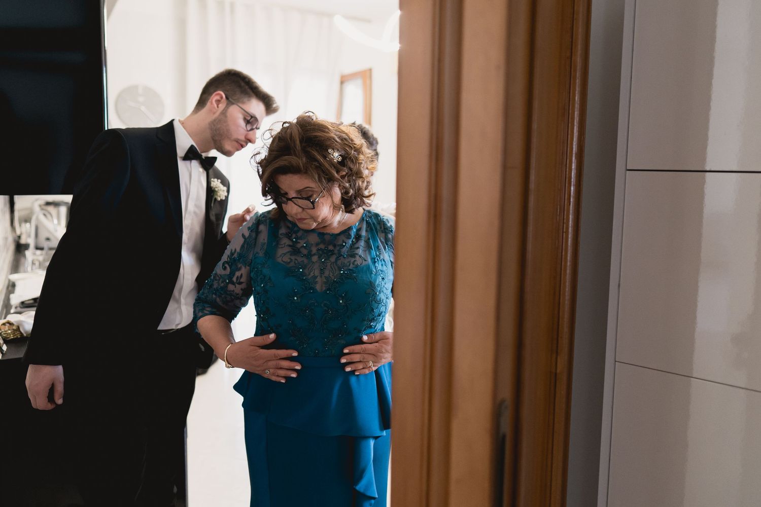 A couple shares an intimate moment in formal attire with the woman wearing a stunning teal lace gown.