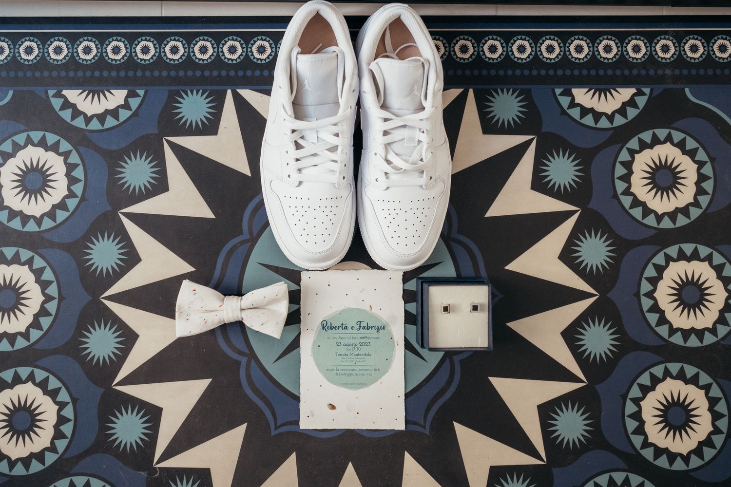 White sneakers and wedding accessories arranged on a patterned blue and gray geometric floor.