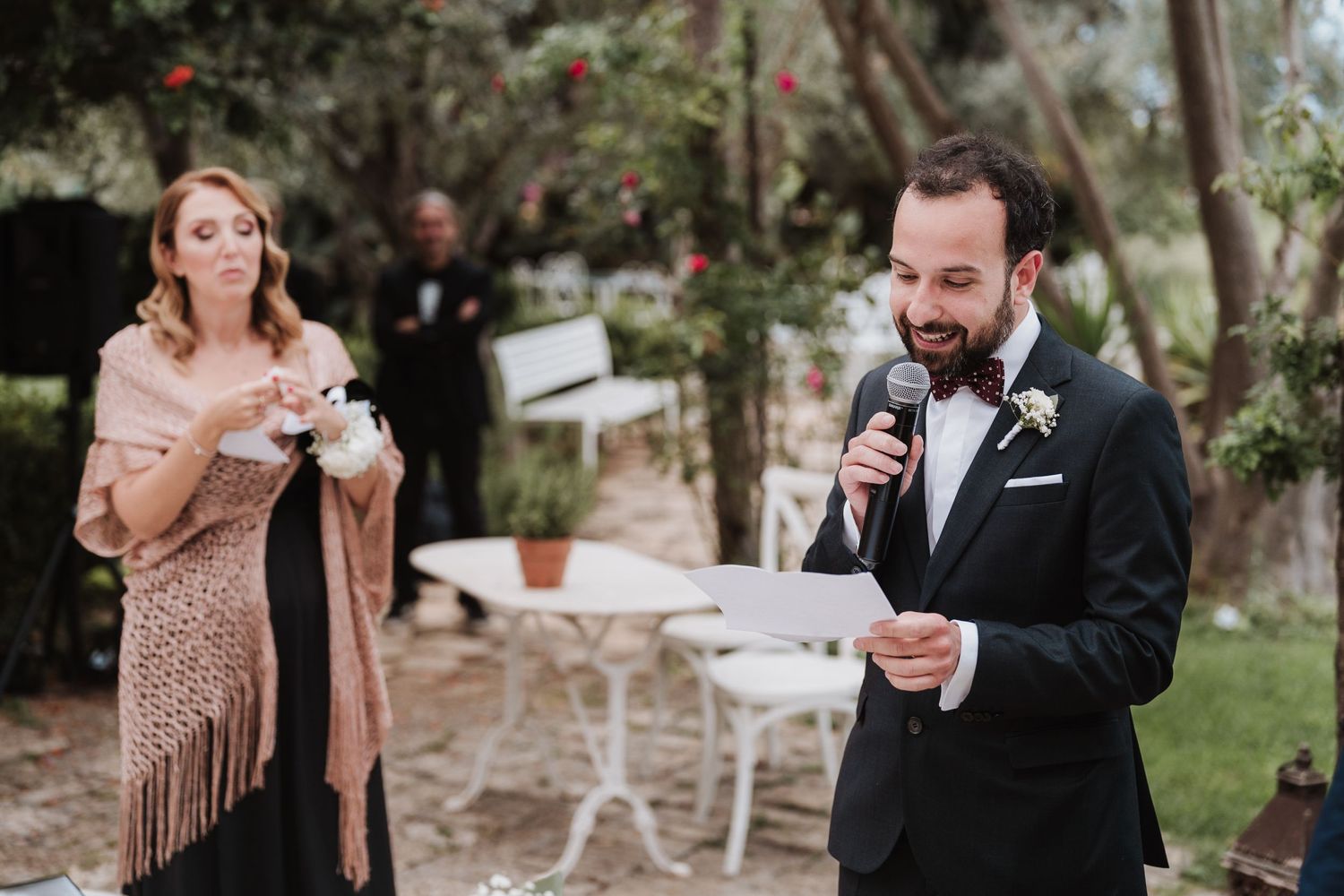 Wedding guests deliver speeches during an outdoor garden reception.