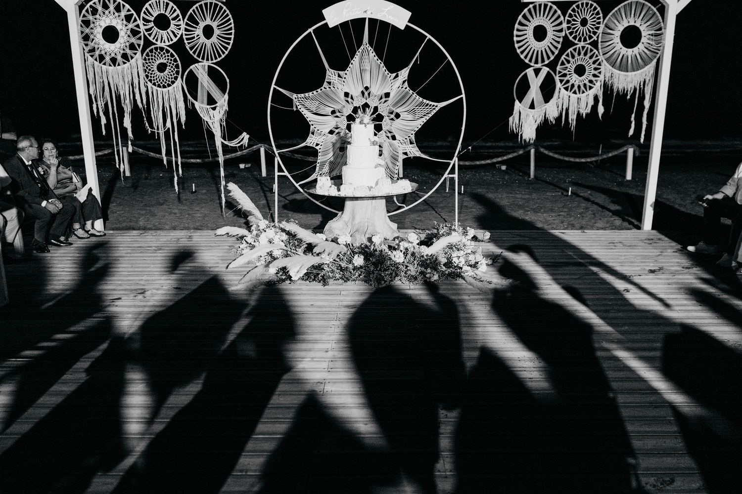Artistic black and white wedding ceremony setup with dreamcatcher decorations casting dramatic shadows.