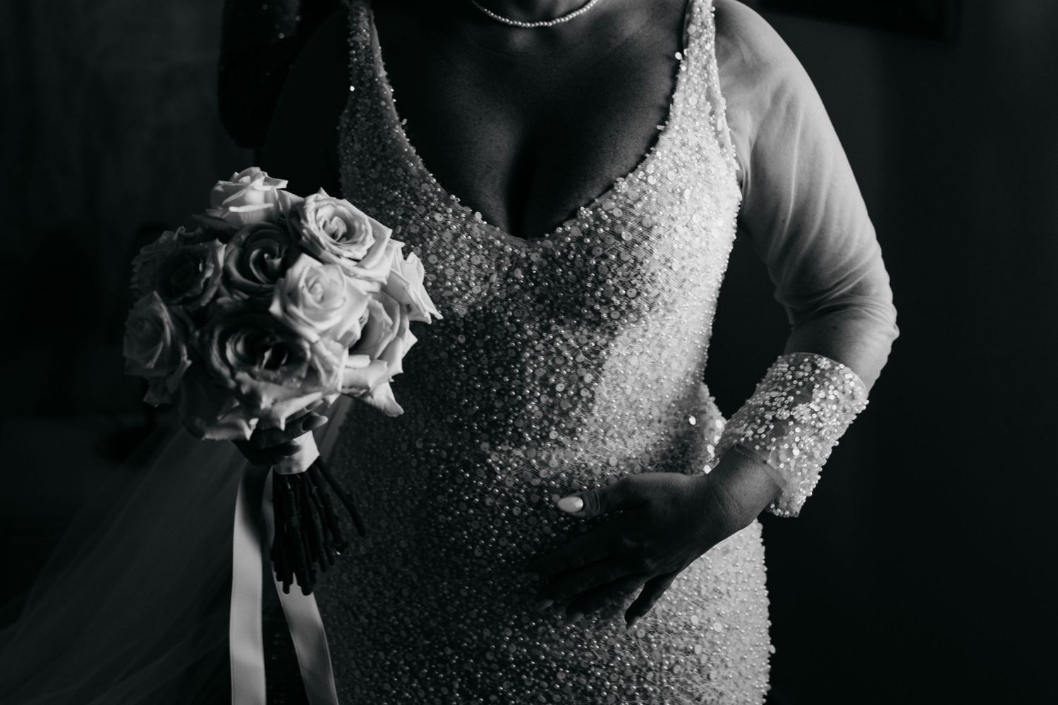 Close-up details of a sparkly wedding dress and floral accessories in monochrome.