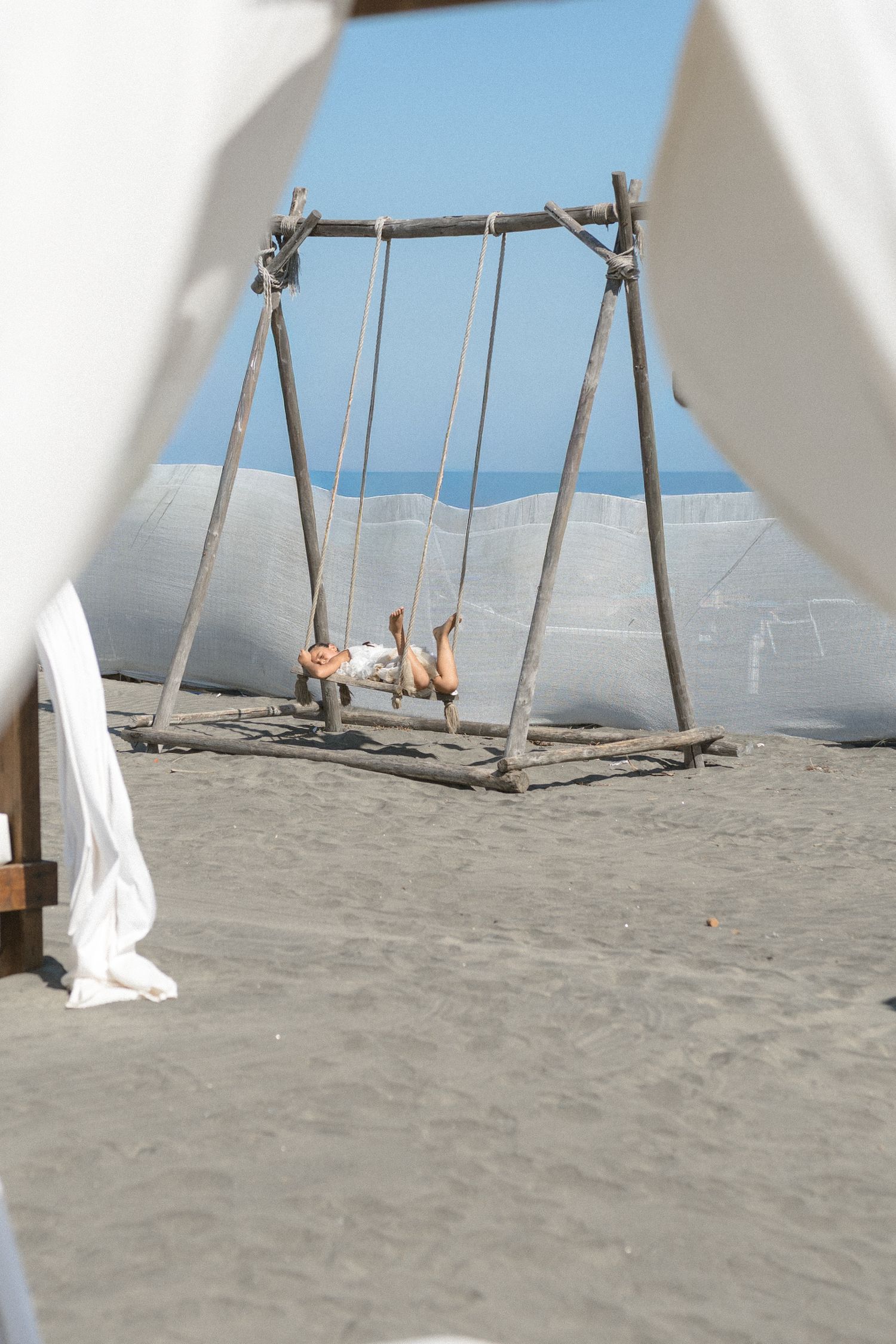 A rustic wooden swing set on a sandy beach with ocean views in the background.