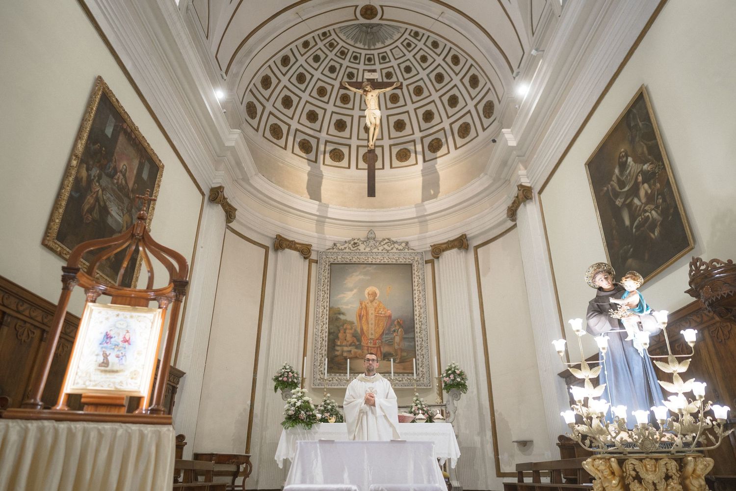 Interior of a church with a domed ceiling, white walls, and religious artwork displayed at the altar.