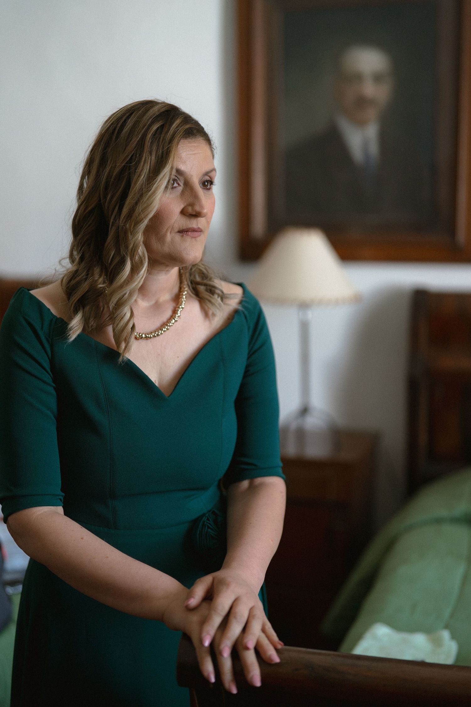 Woman in emerald green dress sitting indoors during formal event.