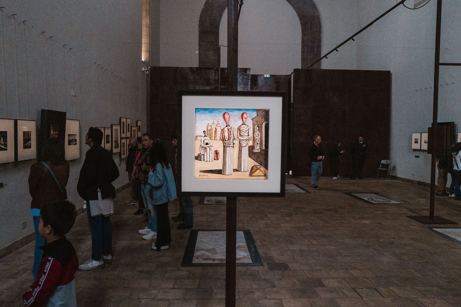 Gallery visitors observe illuminated artwork displays in a dimly lit exhibition space with arched architecture.