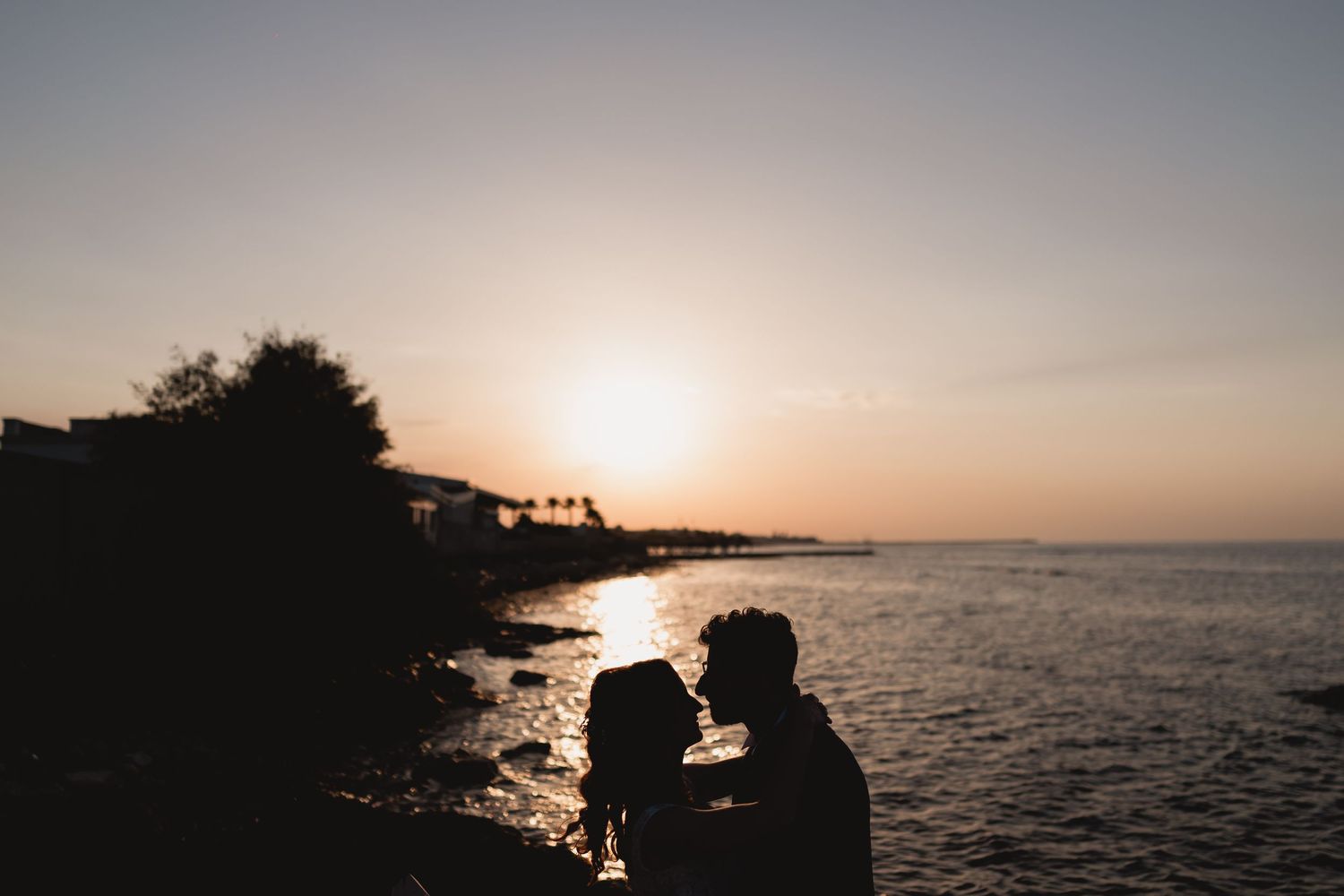 Silhouette of a couple against a sunset over the ocean.
