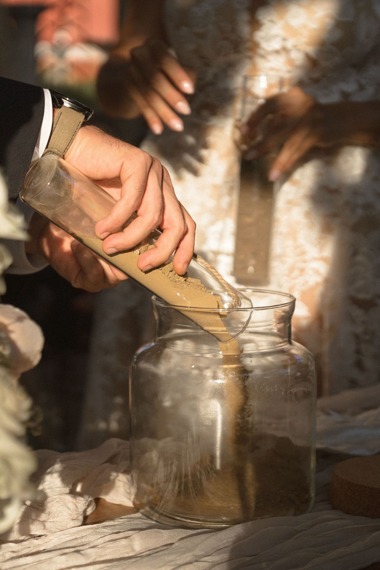 Close-up of hands pouring sand into a glass vessel during a unity ceremony.