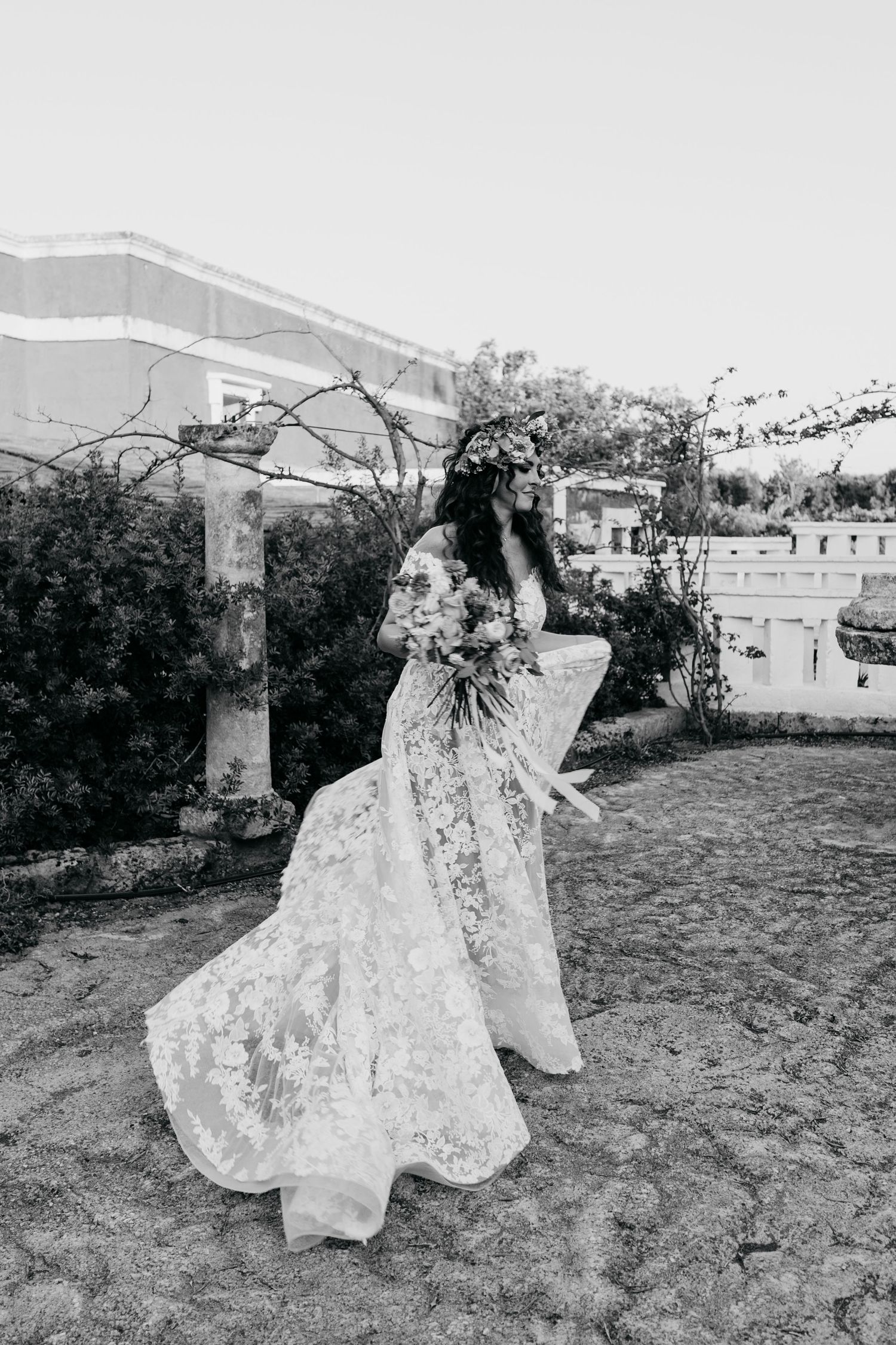 Black and white photo of bride in lace dress twirling in a garden setting.
