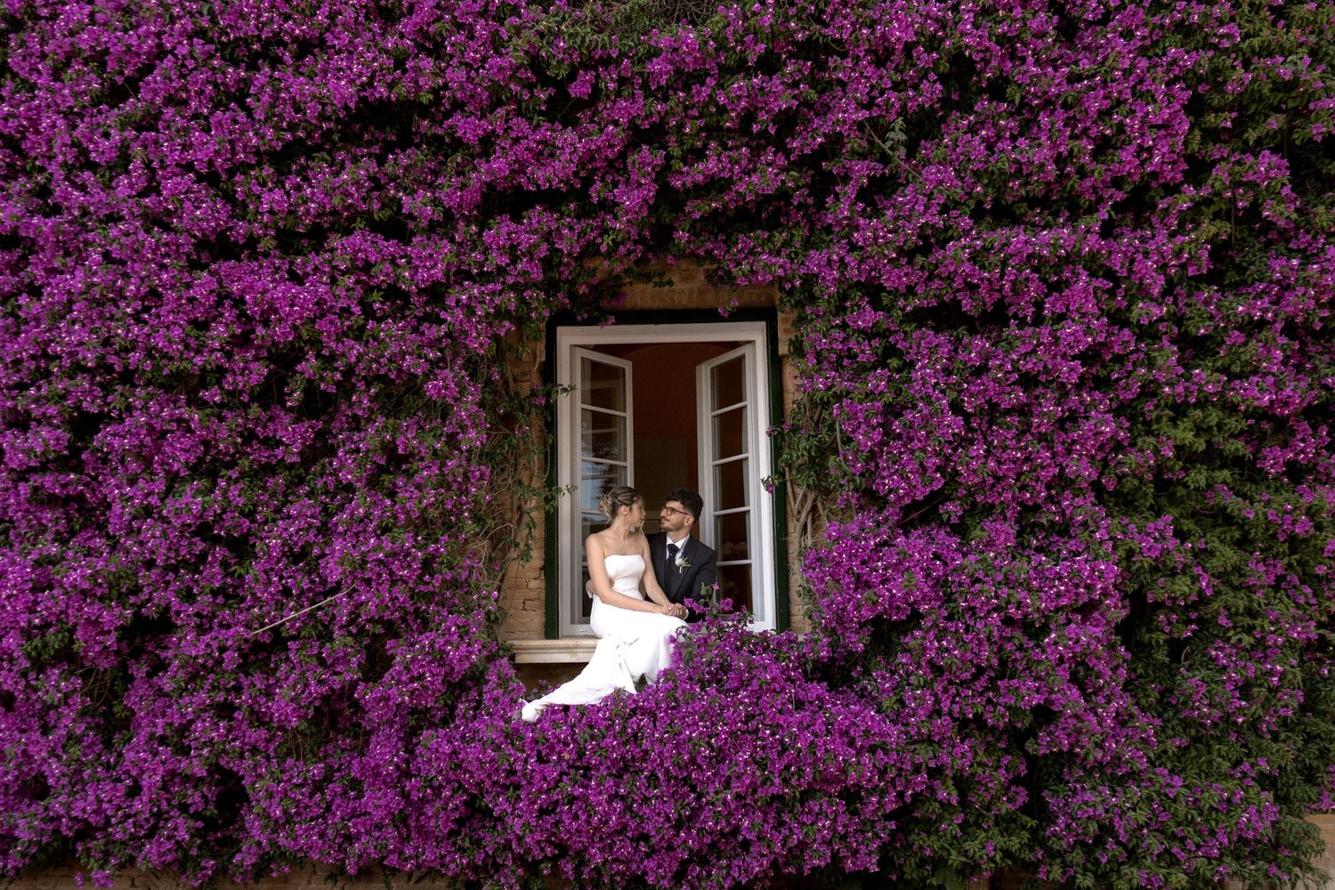 White wedding dress contrasts beautifully against vibrant purple bougainvillea flowers.