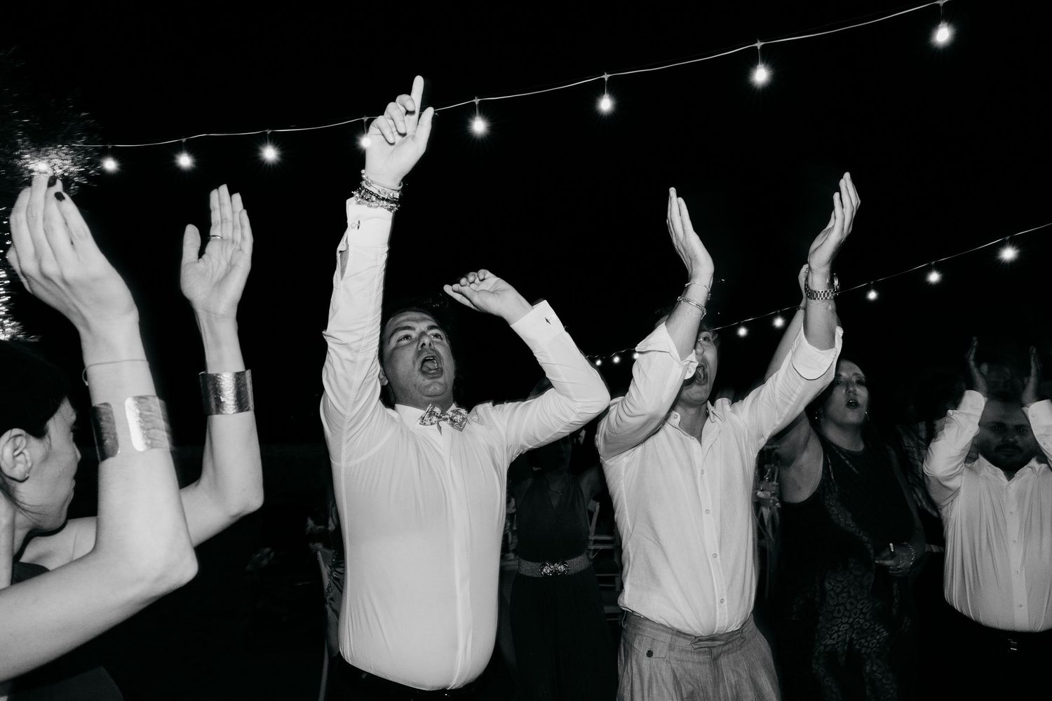 Wedding reception dance floor with string lights overhead and silhouettes of people dancing.