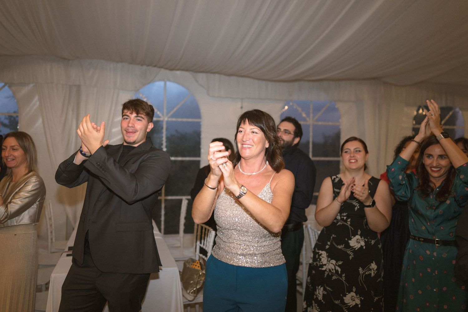 Wedding guests dancing and celebrating under a white tent at an evening reception.