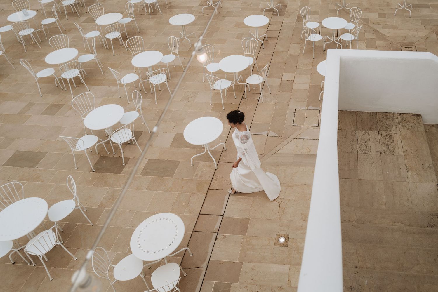 Aerial view of white round tables and chairs arranged on a patio with a person in white walking through.