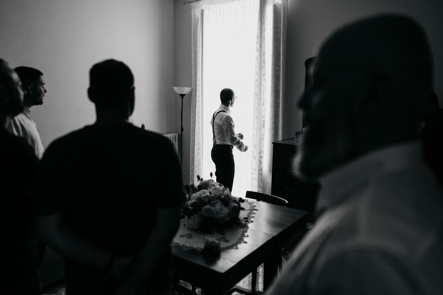 Black and white silhouette of people gathered in room with window light.