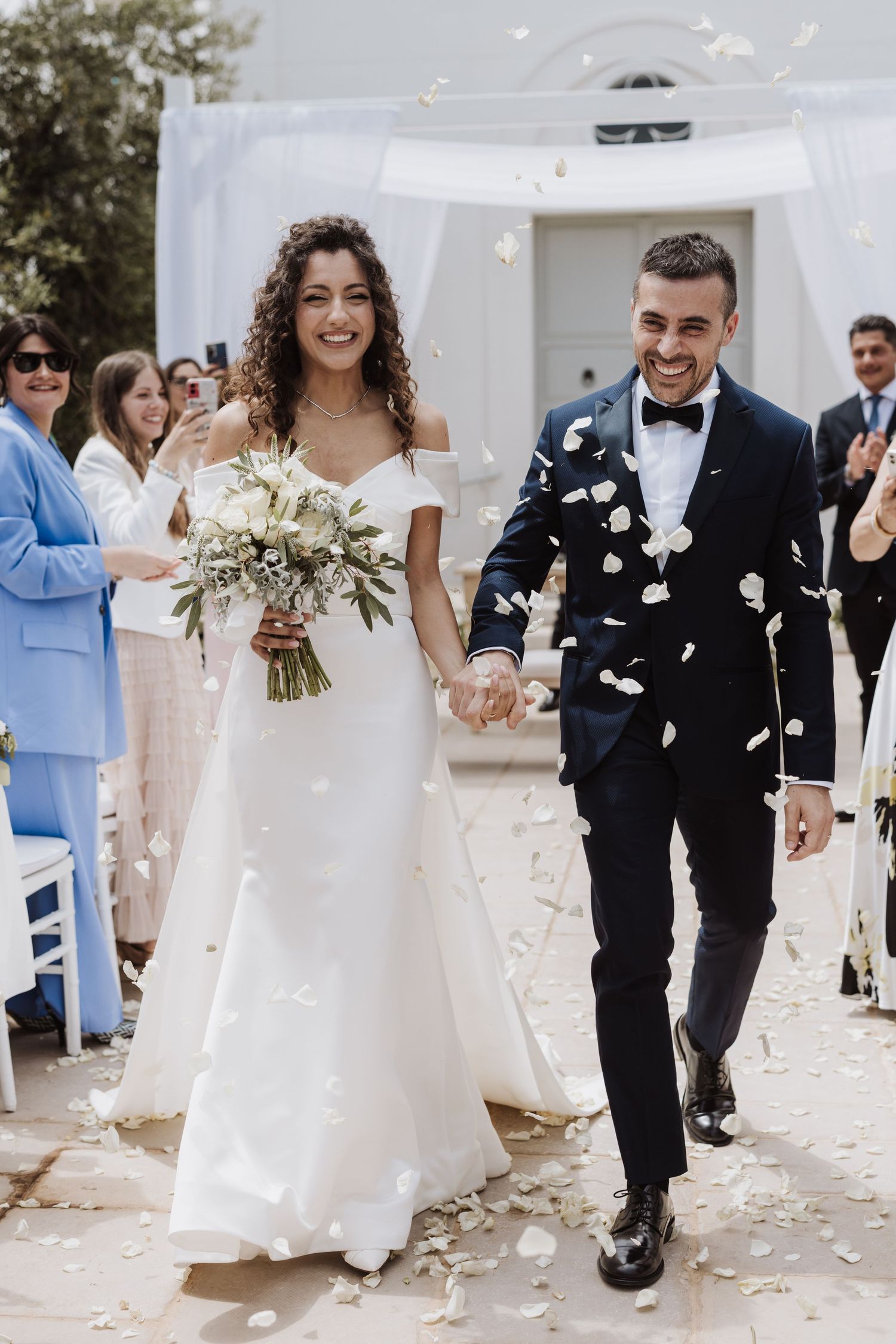 Wedding couple walking down aisle while guests throw white flower petals.