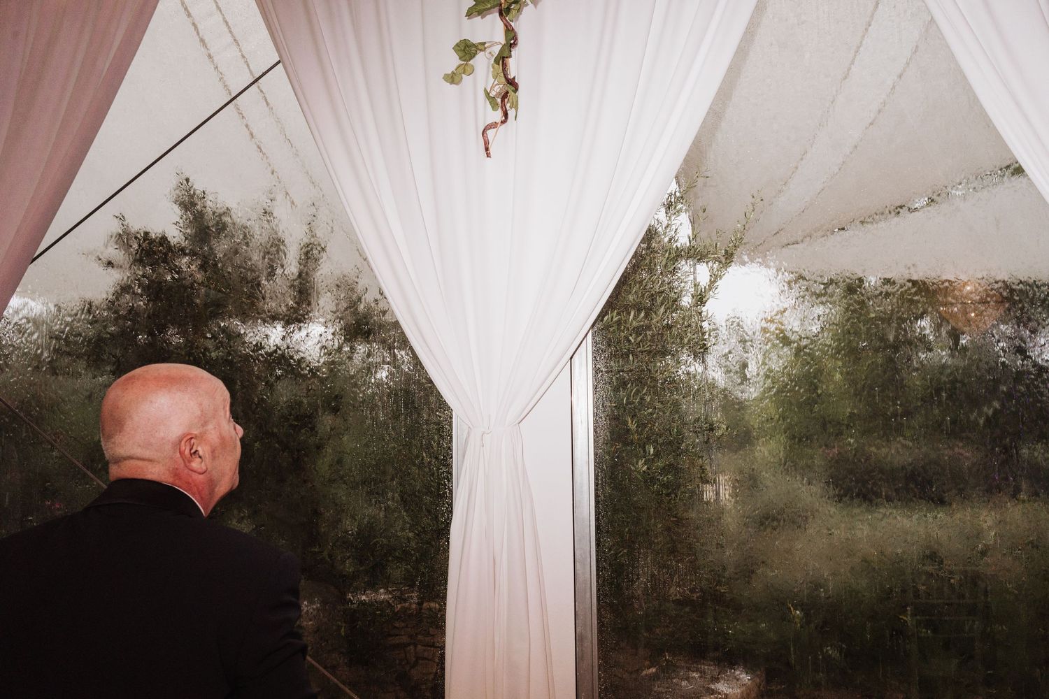 White wedding tent draped with flowing fabric and greenery outdoors.