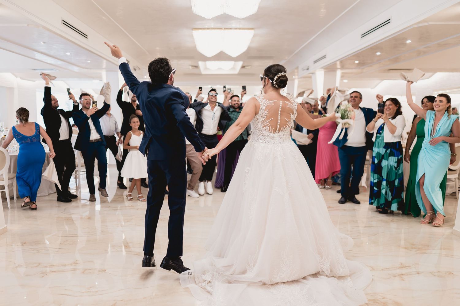 Wedding guests surround a dancing couple in a bright reception hall with modern decor.
