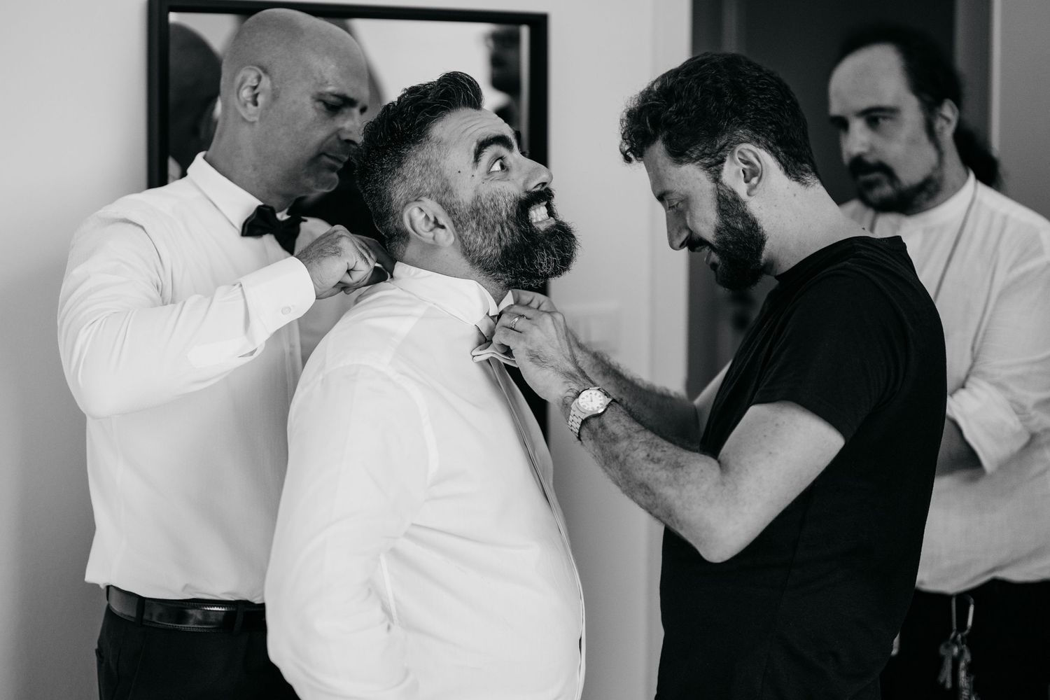 Black and white image of men helping adjust formal attire before an event.