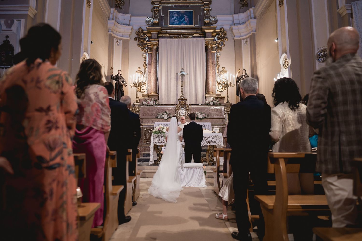 View down the aisle of a church wedding ceremony with ornate architecture and candle lighting.