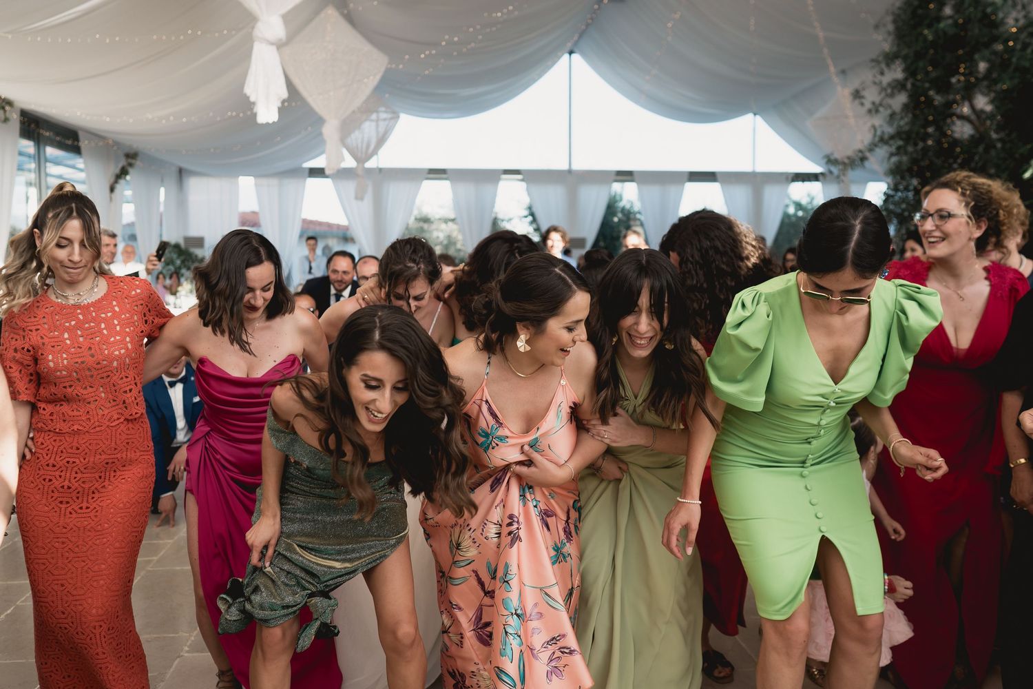 Wedding guests dancing together in colorful dresses at a lively reception party.