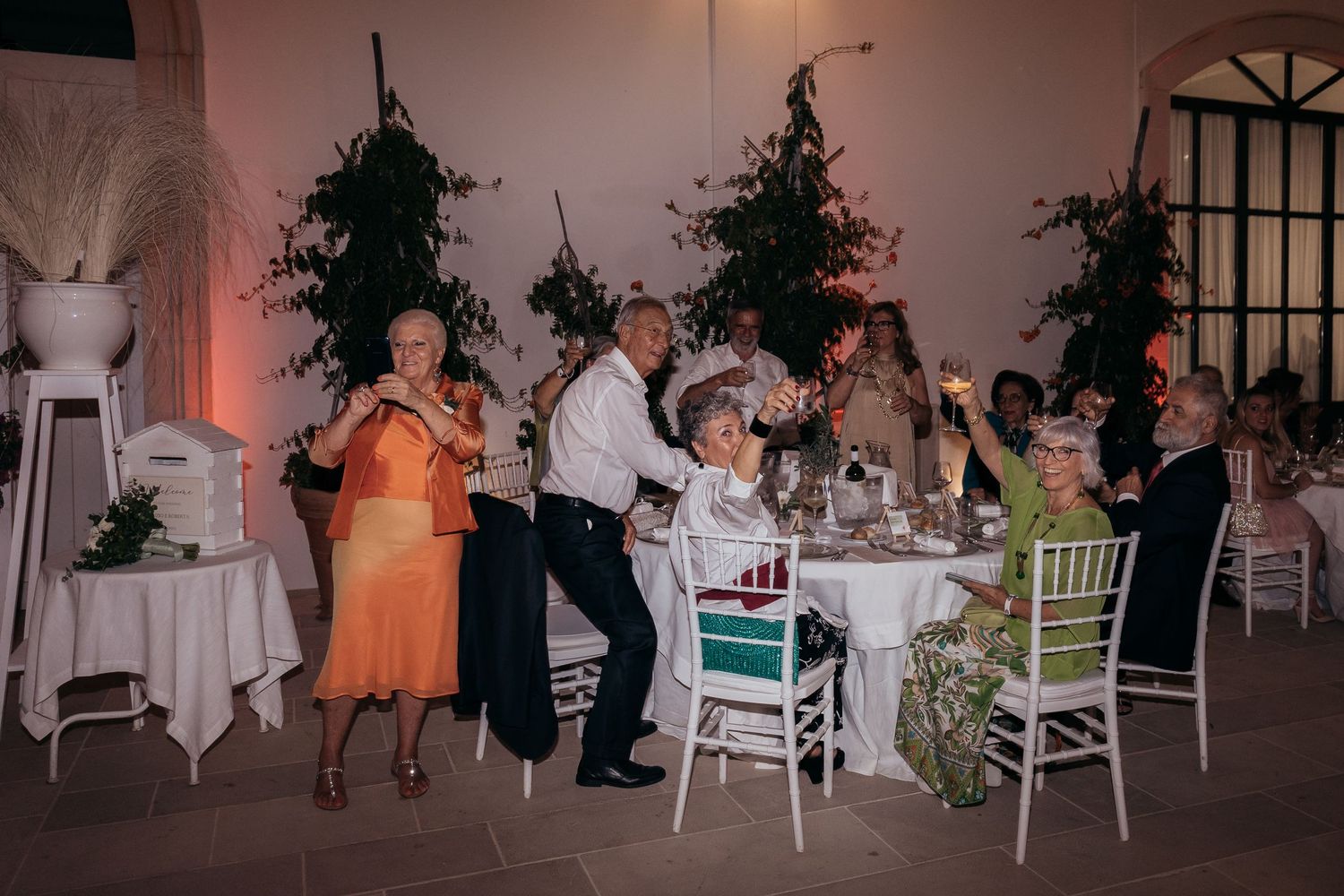 Wedding reception dinner setup with guests seated at decorated tables with hanging plants.