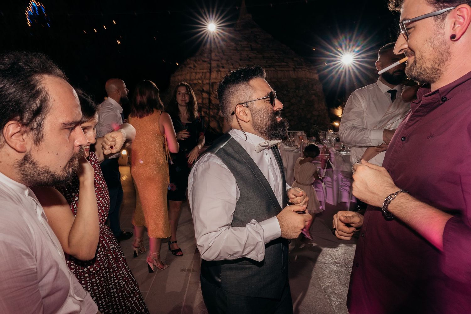 Wedding guests socialize and laugh together during an evening reception celebration.