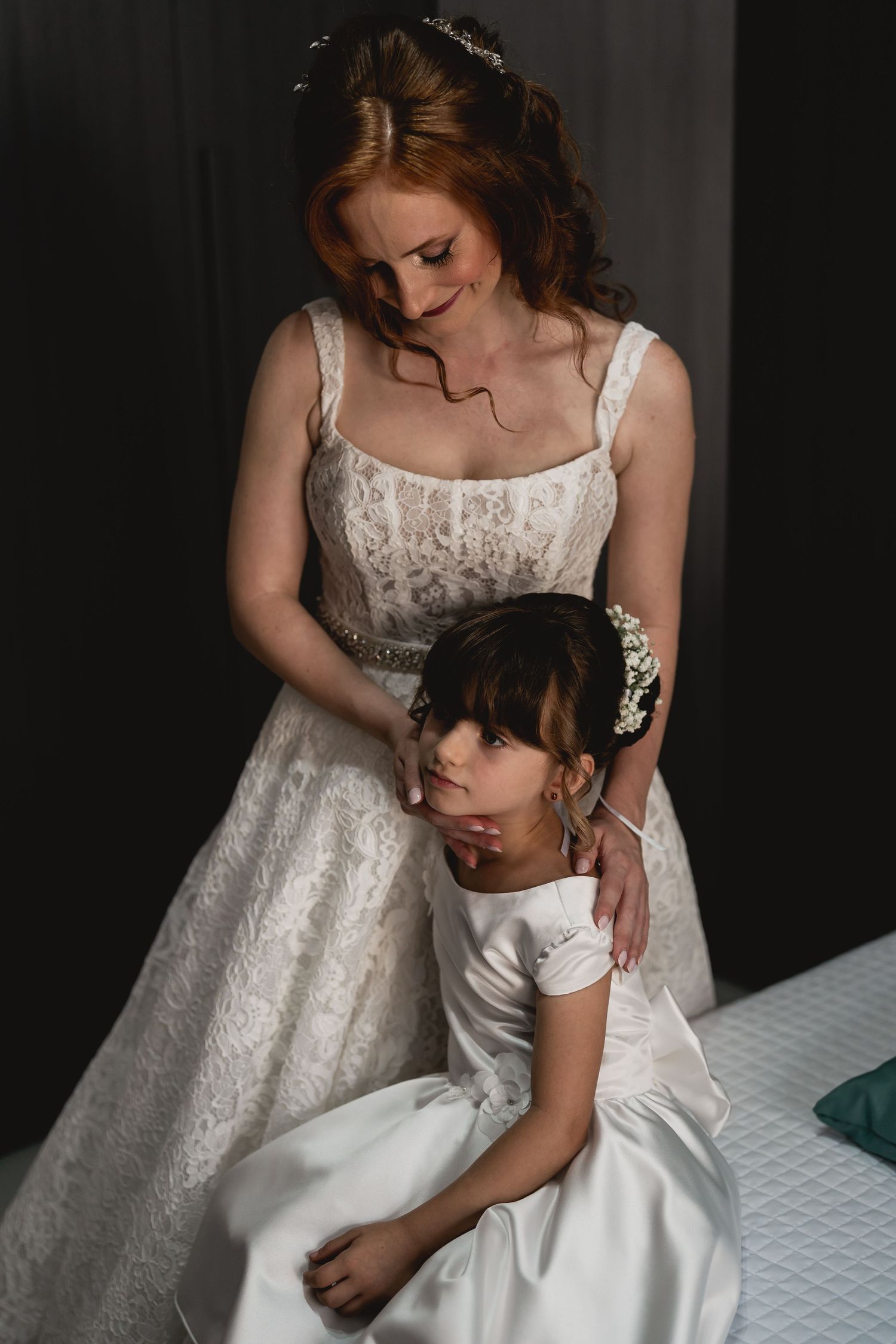 Mother and daughter share an intimate moment in white lace and satin wedding dresses.