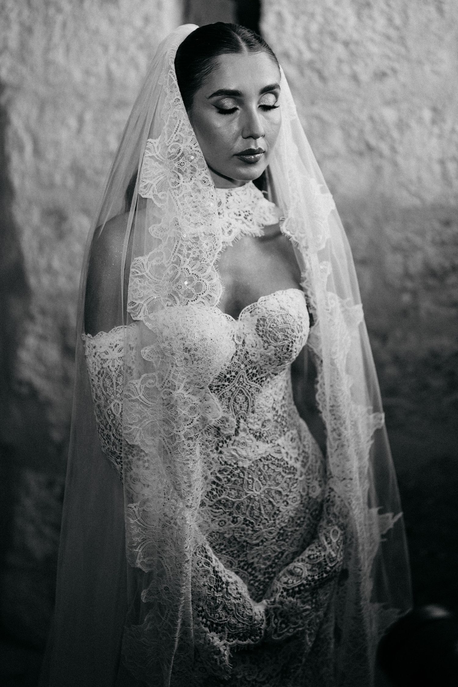 Black and white portrait of a bride in a strapless lace wedding dress and long lace-trimmed veil with her eyes closed.