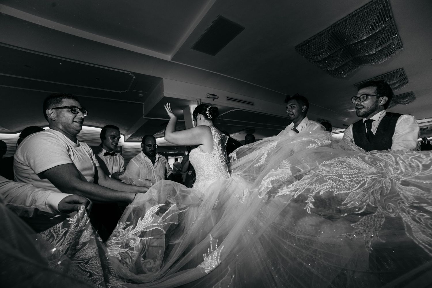 Black and white photo of lively wedding reception with flowing dress in motion.